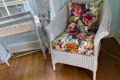 White wicker chair with bright floral cushions in bedroom