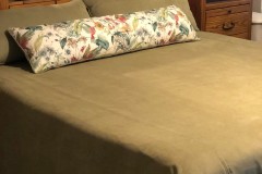 Green suede bedspread with floral bolster pillow on client bed