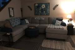 Gray sectional with round ottoman and teal pillows in client living room