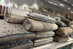 Showroom display of stacked designer pillows, bolsters, and fabric samples in neutral tones